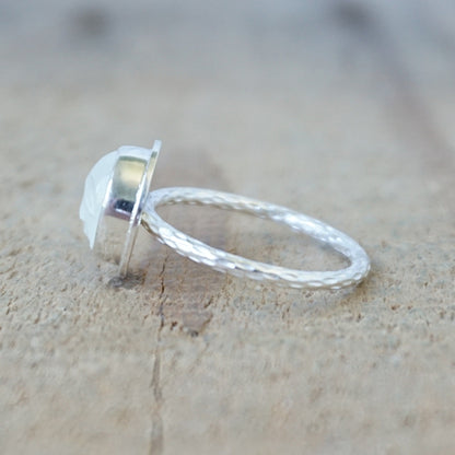 side view of a silver ring with a round white stone with a carved face, against a wooden background