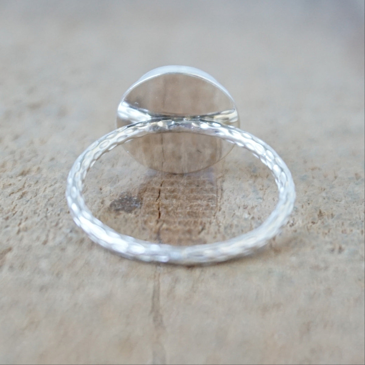 back view of a silver ring with a round white stone with a carved face, against a wooden background