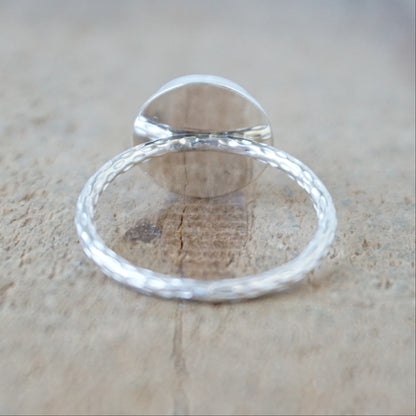 back view of a silver ring with a round white stone with a carved face, against a wooden background