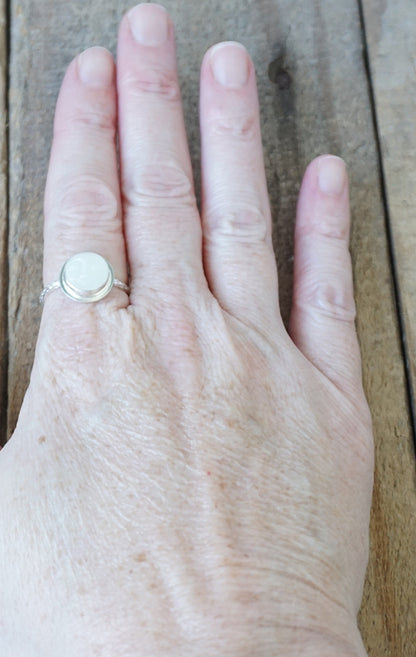 hand wearing a silver ring with a round white stone with a carved face, against a wooden background