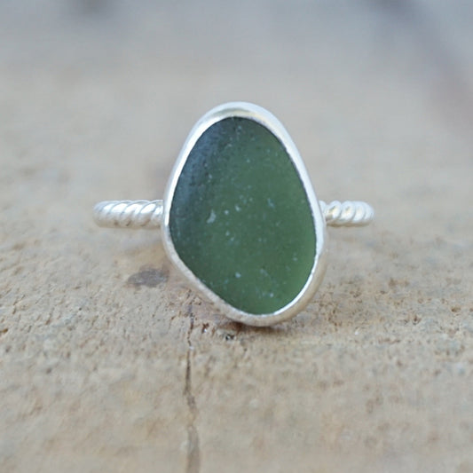 silver ring with a piece of green sea glass, against a wooden background