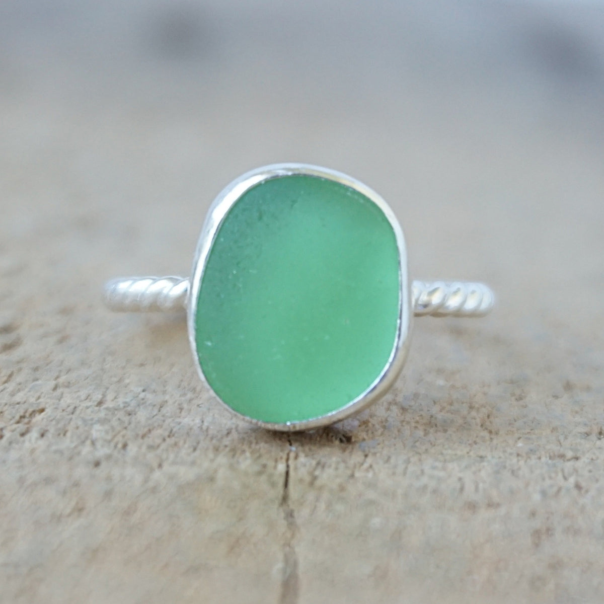 silver ring with a piece of green sea glass, against a wooden background