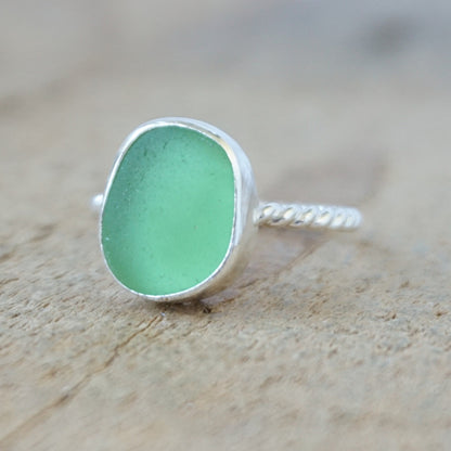 silver ring with a piece of green sea glass, against a wooden background