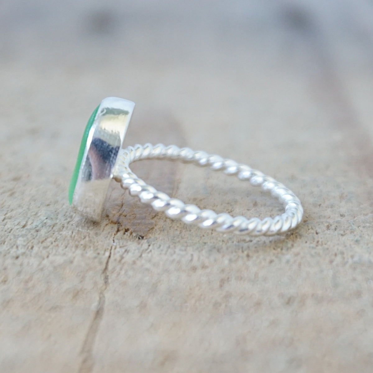 side view of a silver ring with a piece of green sea glass, against a wooden background