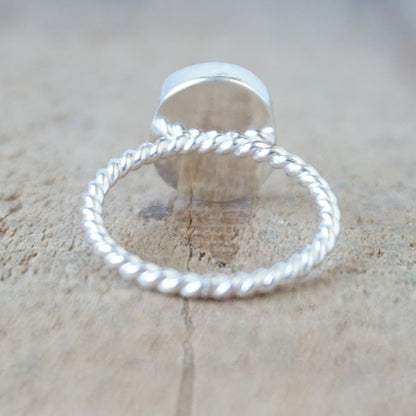 back view of a silver ring with a piece of green sea glass, against a wooden background