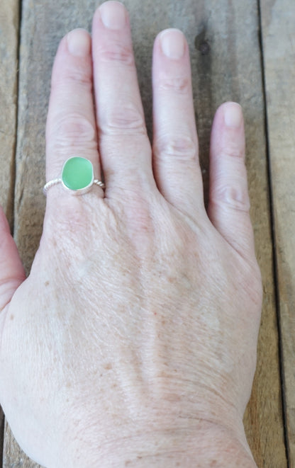hand wearing a silver ring with a piece of green sea glass, against a wooden background