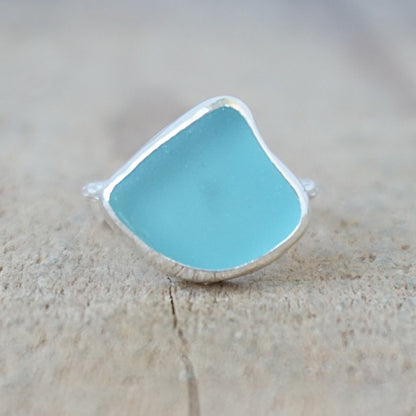 silver ring with a piece of teal blue sea glass, against a wooden background