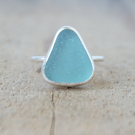 silver ring with a piece of teal blue sea glass, against a wooden background