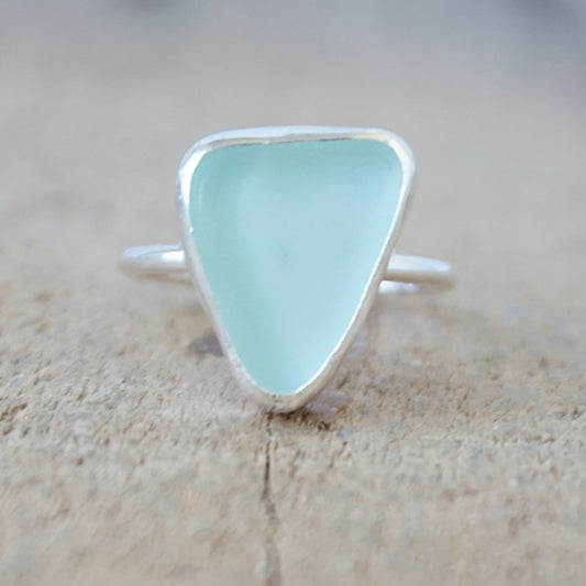 silver ring with a piece of seafoam green sea glass, against a wooden background