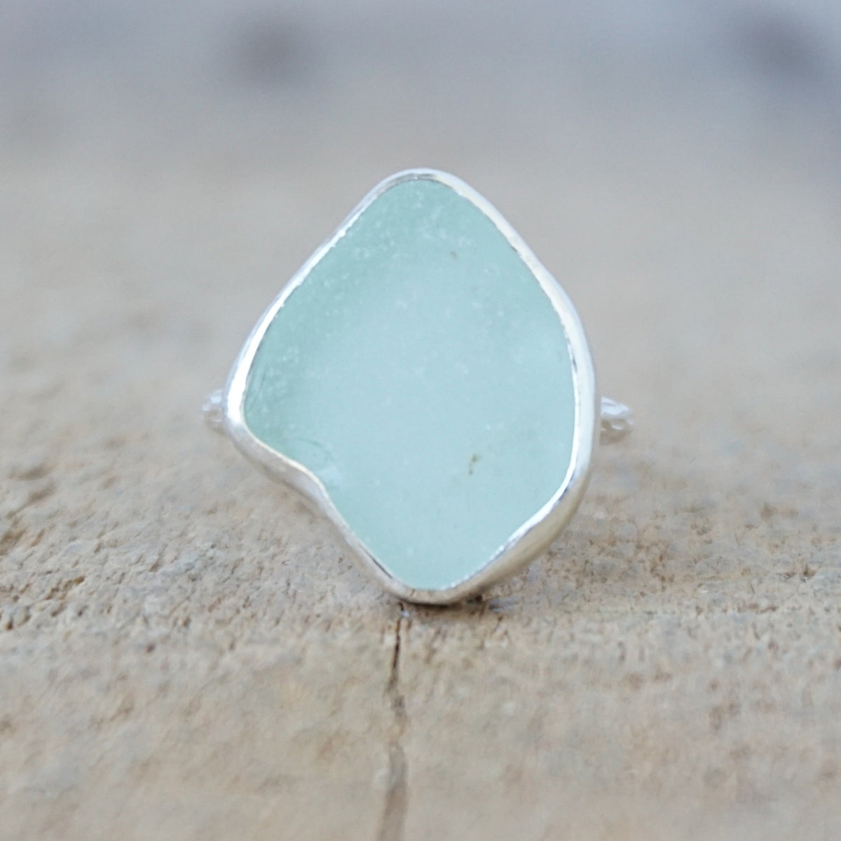silver ring with a piece of seafoam green sea glass, against a wooden background