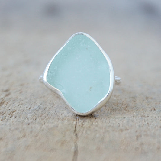 silver ring with a piece of seafoam green sea glass, against a wooden background