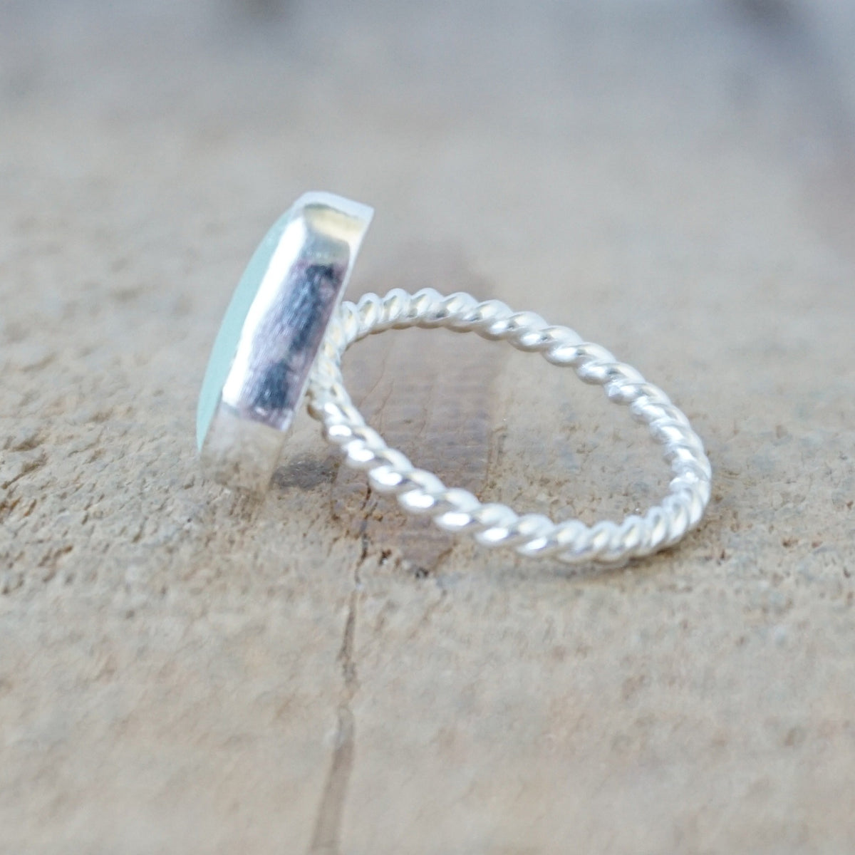 side view of a silver ring with a piece of seafoam green sea glass, against a wooden background