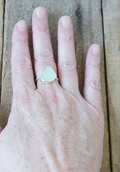 hand wearing a silver ring with a piece of seafoam green sea glass, against a wooden background