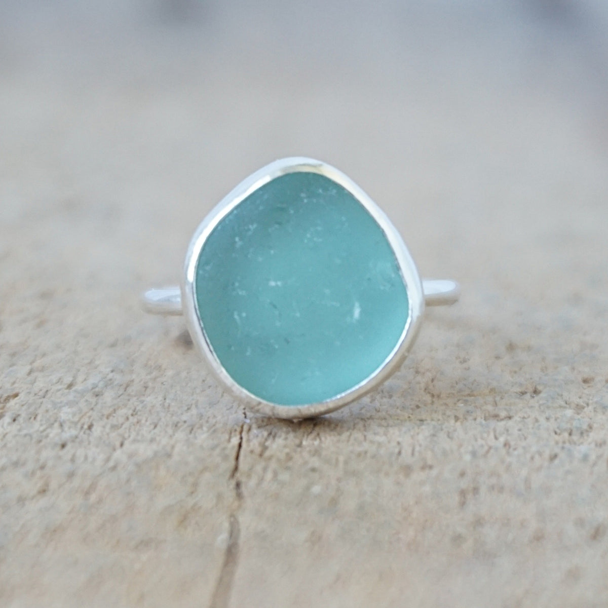 silver ring with a piece of teal blue sea glass, against a wooden background