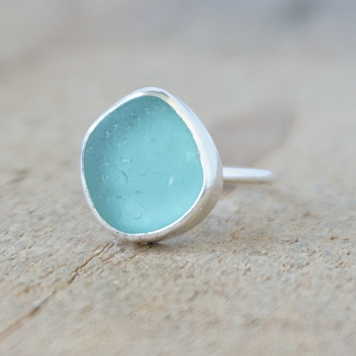 silver ring with a piece of teal blue sea glass, against a wooden background