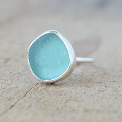 silver ring with a piece of teal blue sea glass, against a wooden background