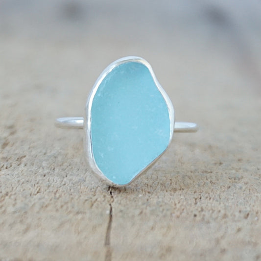 silver ring with a piece of light blue sea glass, against a wooden background