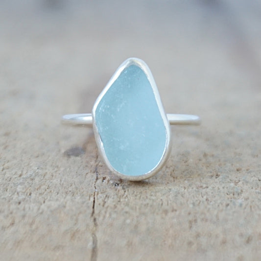 silver ring with a piece of light blue sea glass, against a wooden background