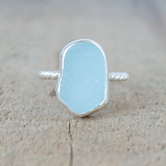 silver ring with a piece of light blue sea glass, against a wooden background