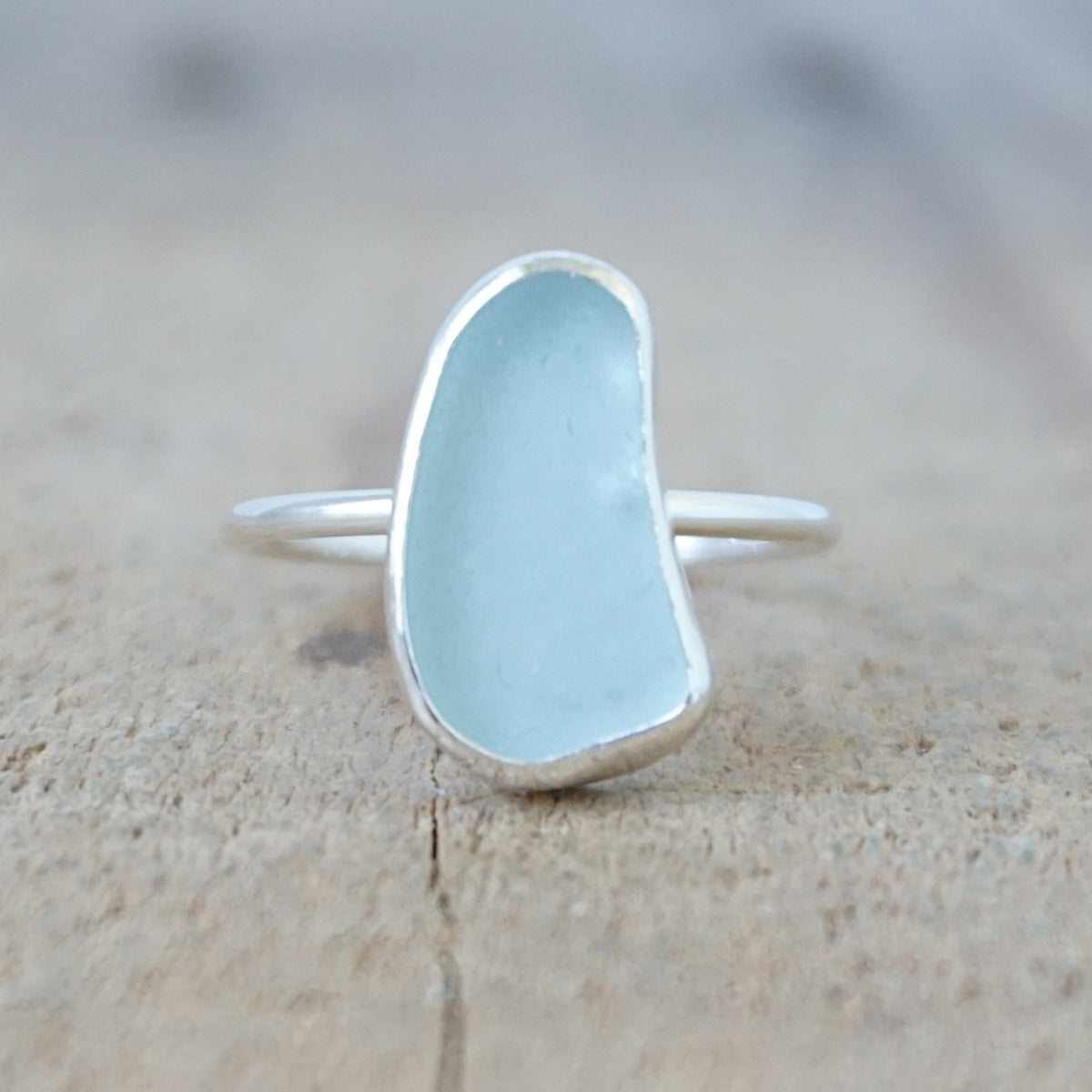 silver ring with a piece of light blue sea glass, against a wooden background