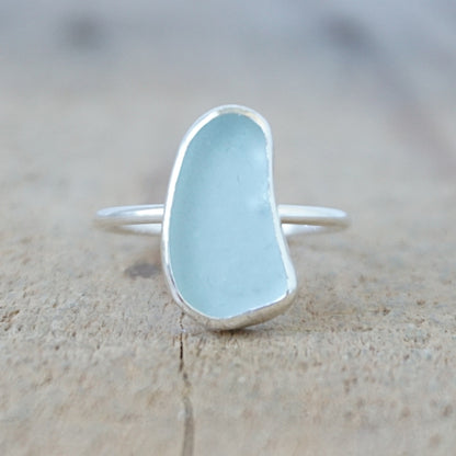 silver ring with a piece of light blue sea glass, against a wooden background