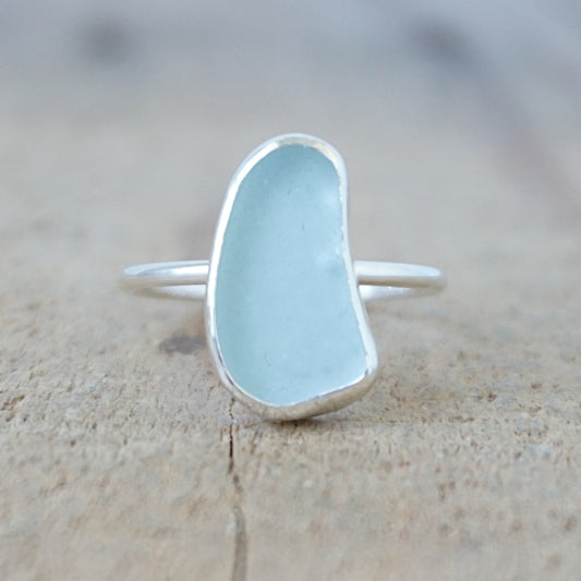 silver ring with a piece of light blue sea glass, against a wooden background