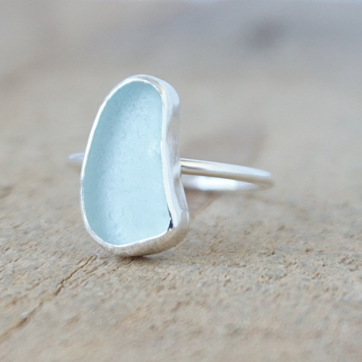 silver ring with a piece of light blue sea glass, against a wooden background