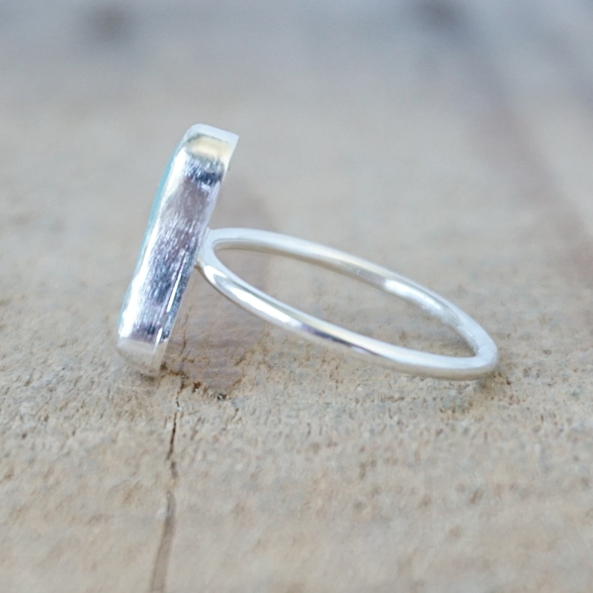side view of a silver ring with a piece of light blue sea glass, against a wooden background