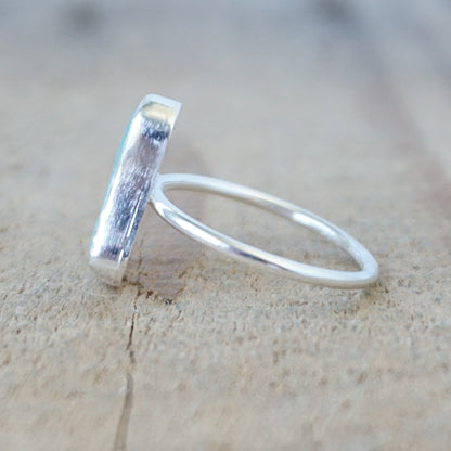 side view of a silver ring with a piece of light blue sea glass, against a wooden background