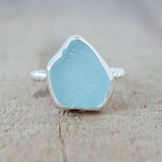 silver ring with a piece of light blue sea glass, against a wooden background