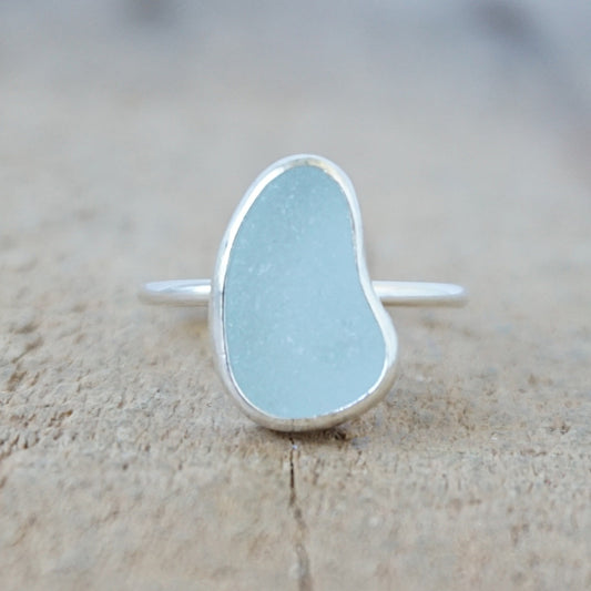 silver ring with a piece of light blue sea glass, against a wooden background
