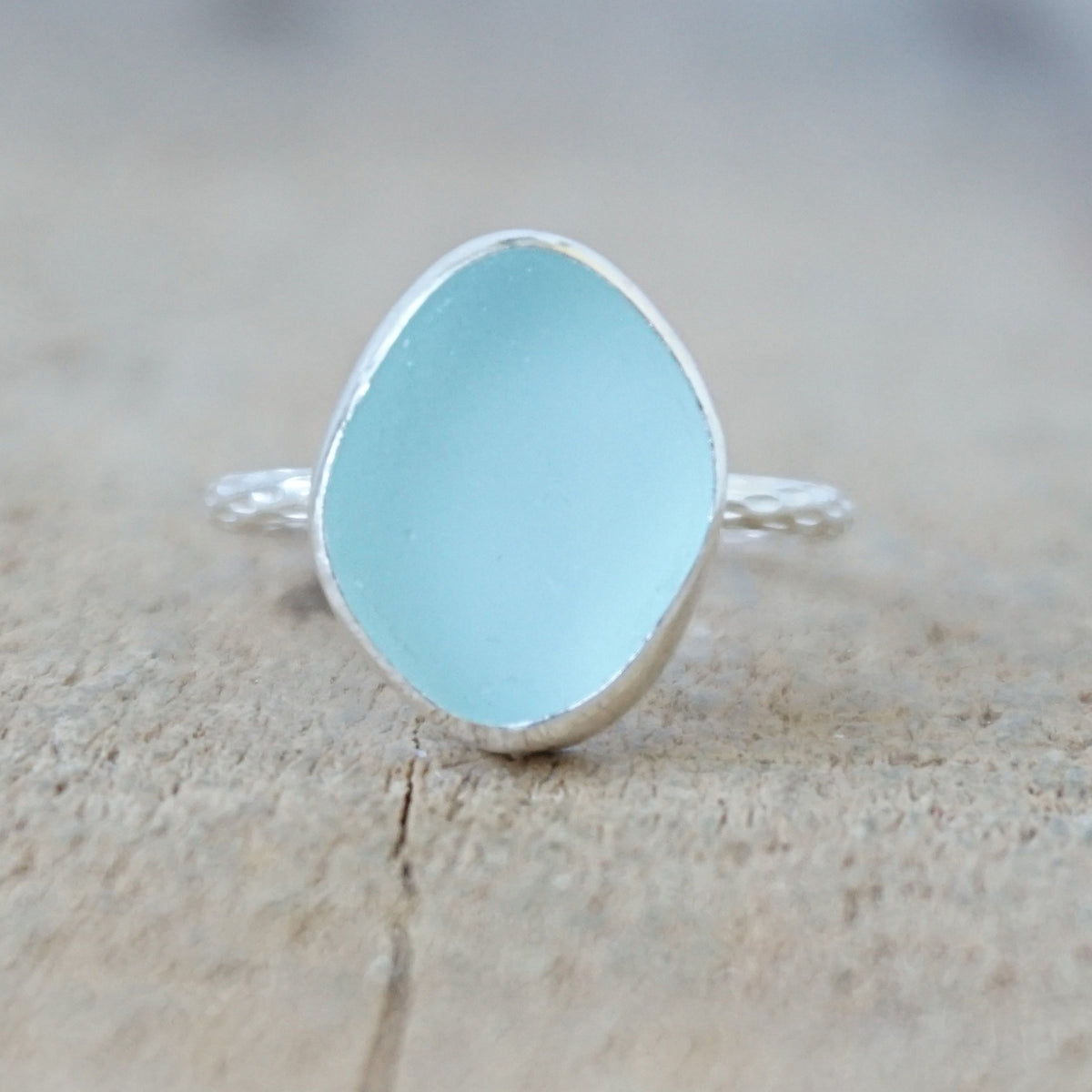 silver ring with a piece of light blue sea glass, against a wooden background
