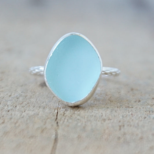 silver ring with a piece of light blue sea glass, against a wooden background
