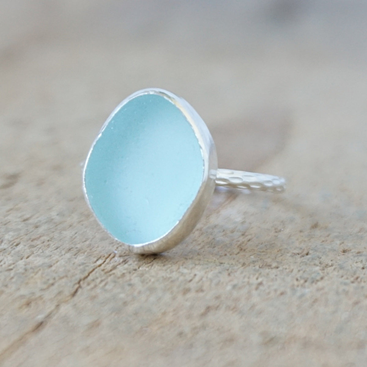 silver ring with a piece of light blue sea glass, against a wooden background