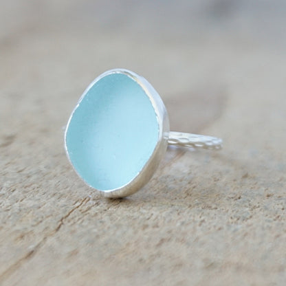 silver ring with a piece of light blue sea glass, against a wooden background