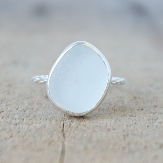 silver ring with a piece of frosted clear sea glass, against a wooden background