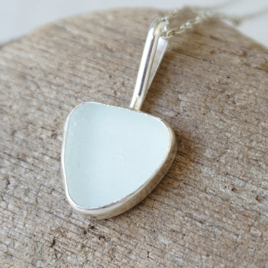 silver pendant with light blue sea glass, against a wooden background