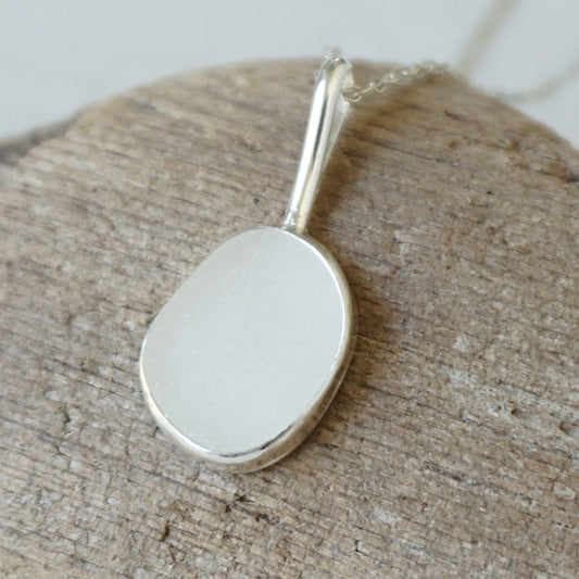 silver pendant with frosted clear sea glass, against a wooden background