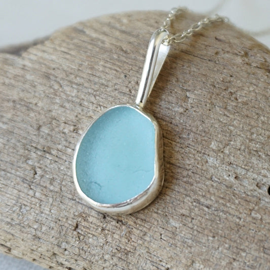 silver pendant with teal blue sea glass, against a wooden background