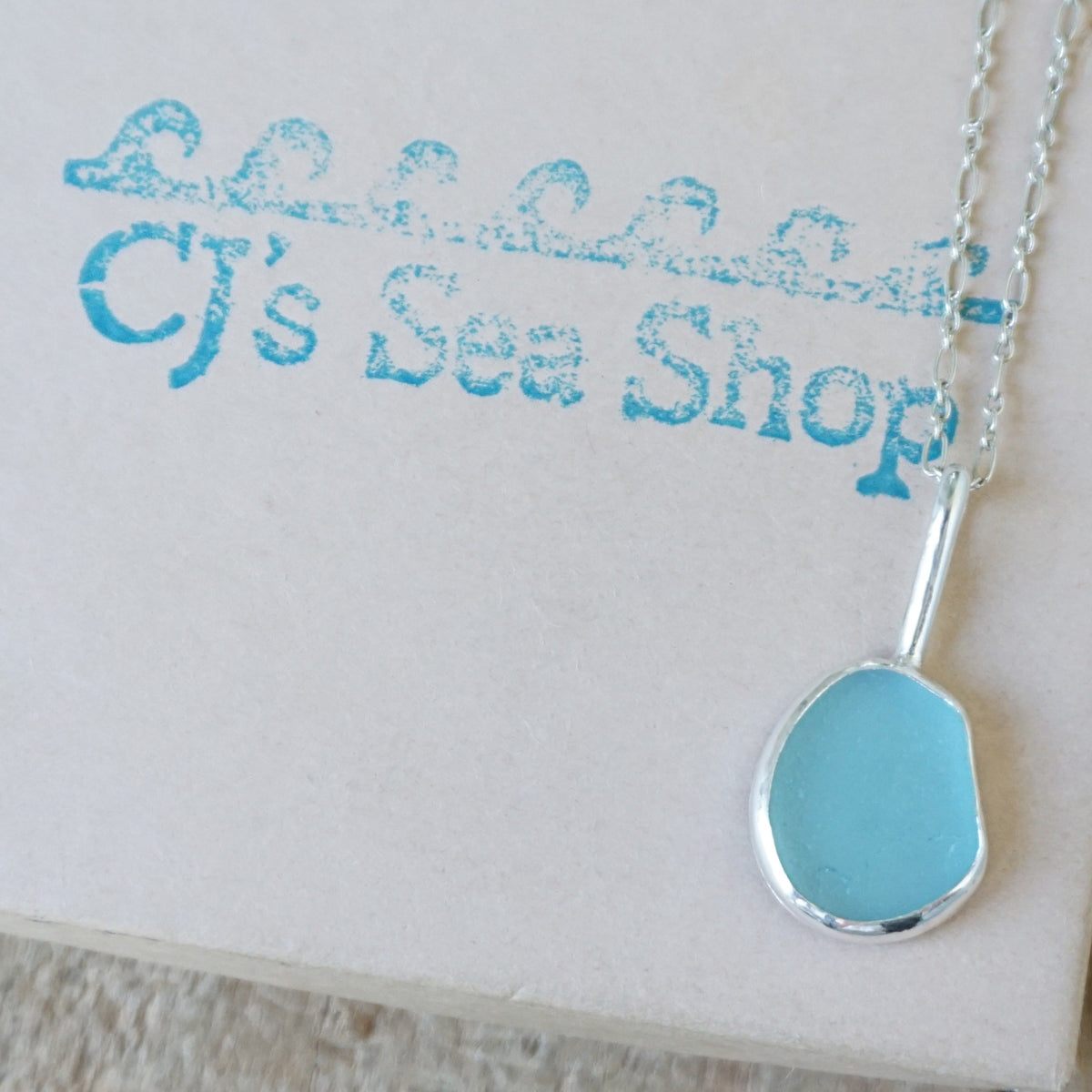 silver pendant with teal blue sea glass, displayed on a gift box
