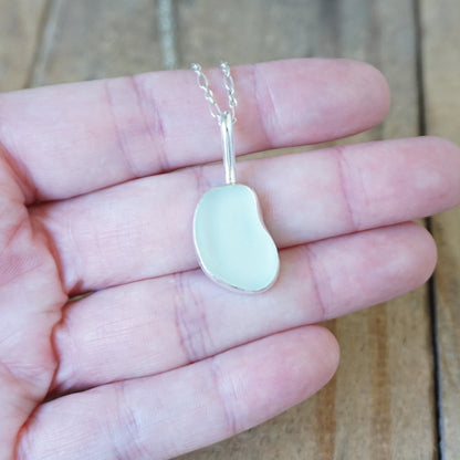 hand holding a silver pendant with seafoam green sea glass, against a wooden background