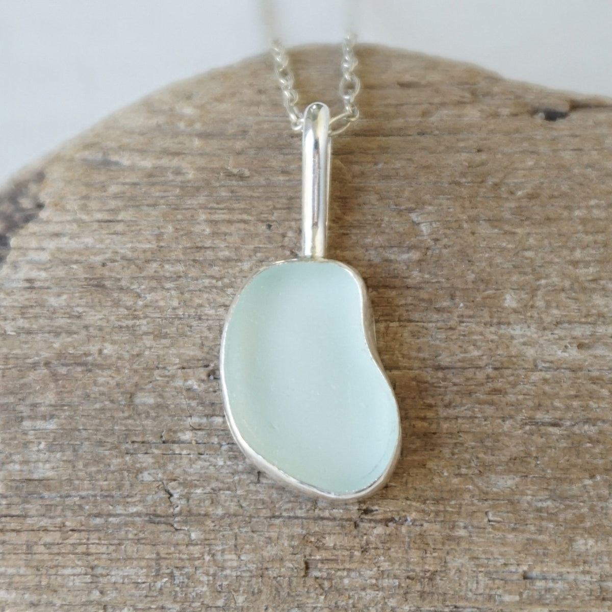 silver pendant with seafoam green sea glass, against a wooden background