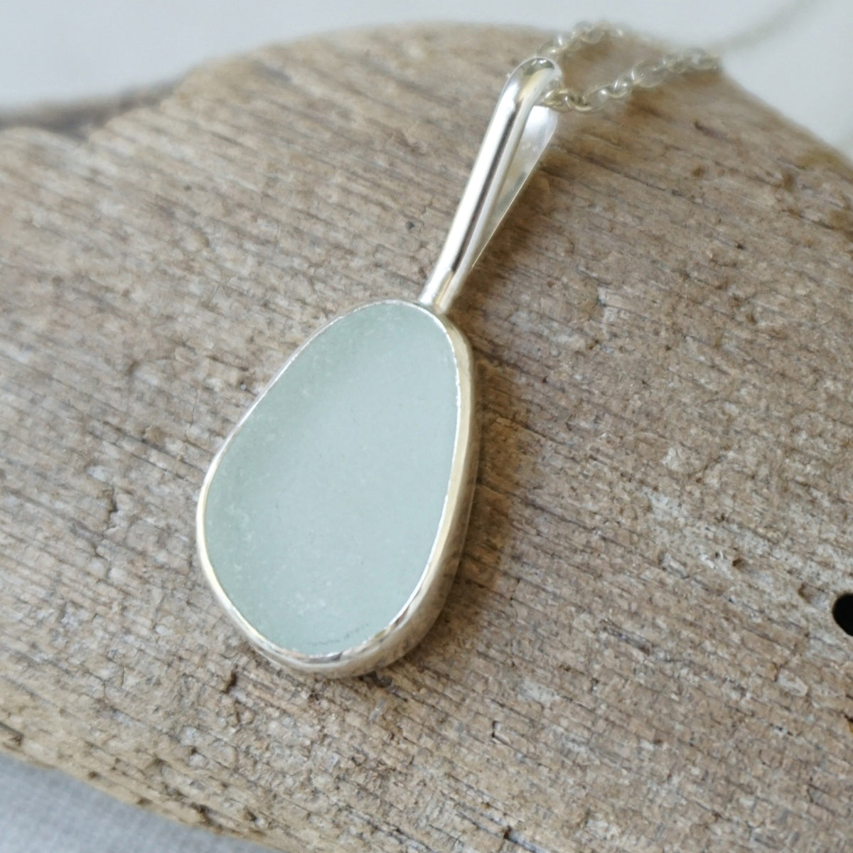 silver pendant with seafoam green sea glass, against a wooden background