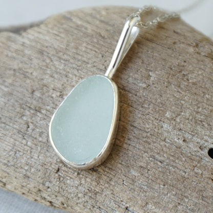 silver pendant with seafoam green sea glass, against a wooden background