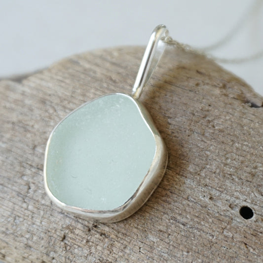 silver pendant with seafoam green sea glass, against a wooden background