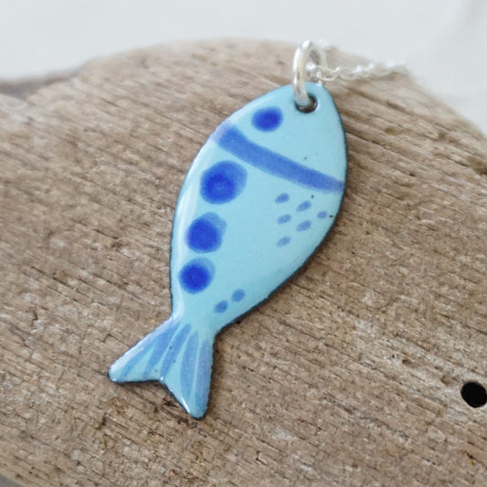 blue enamel fish shaped pendant, against a wooden background
