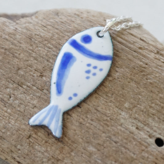 white and blue enamel fish shaped pendant, against a wooden background