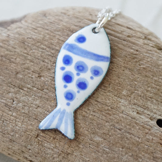 white and blue enamel fish shaped pendant, against a wooden background