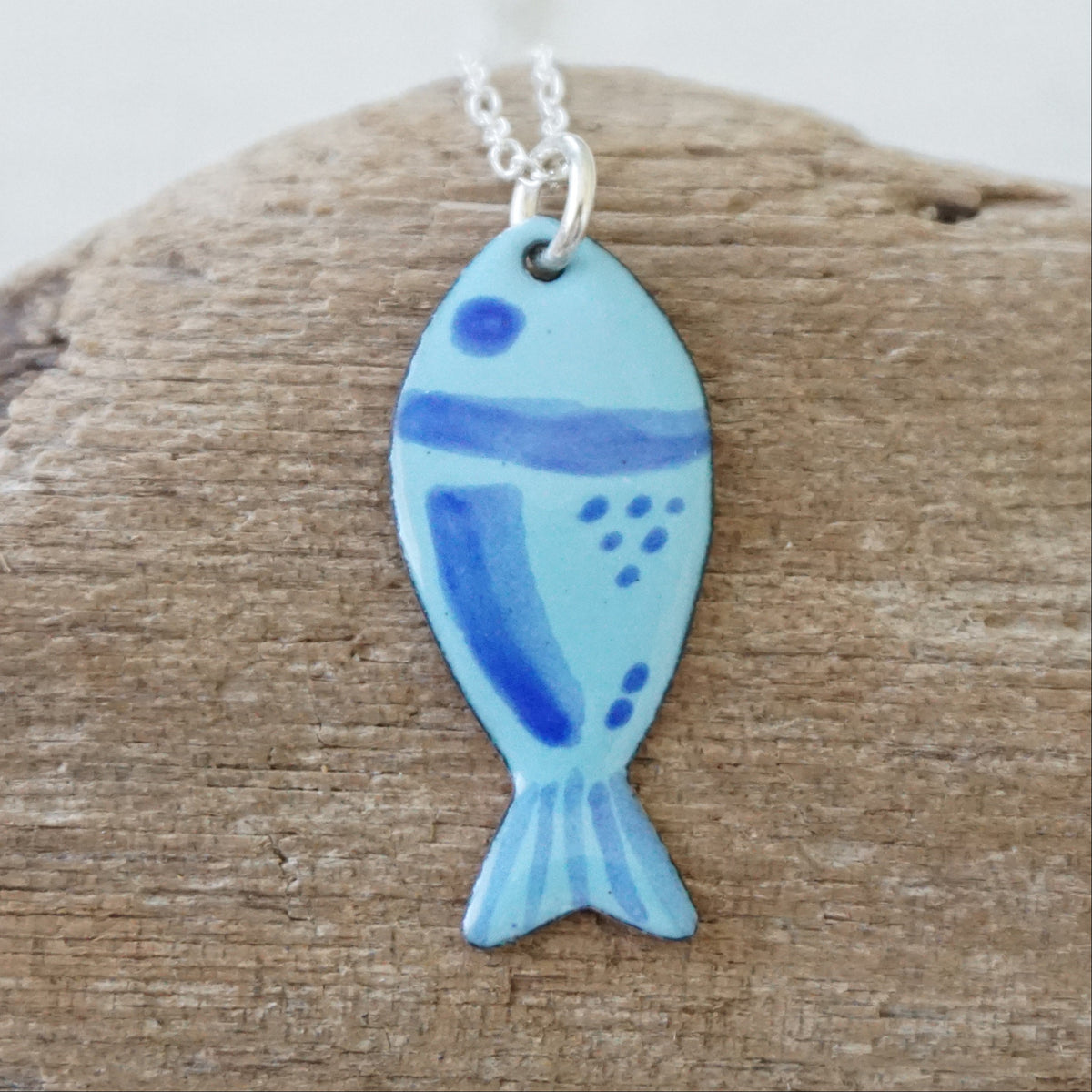 blue enamel fish shaped pendant, against a wooden background