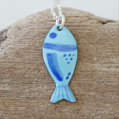 blue enamel fish shaped pendant, against a wooden background